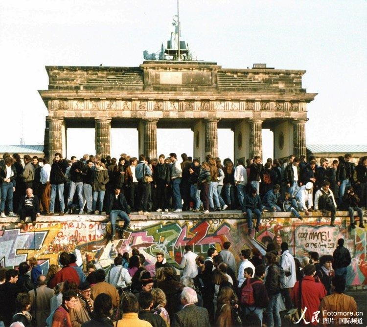 1989年11月10日，德国，柏林：柏林墙开放第二天，来自东西部的德国人站在勃兰登堡门前的柏林墙上。
