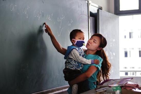 5月7日，汉寿一中。因为图图有些不舒服，一个人坐在教室角落的椅子上总不安静，怕影响到学生们听课，张薇暂时抱着图图在上课。 组图/潇湘晨报记者陈正